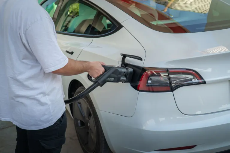 Carro elétrico compacto branco carregando na tomada de uma garagem residencial
