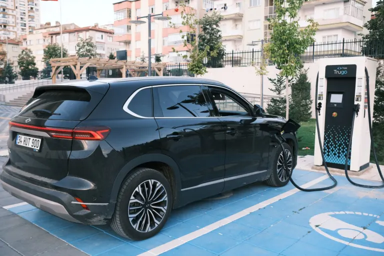 SUV elétrico MG IM6 estacionado em rua urbana ao lado de um ponto de recarga
